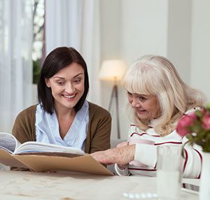 Valuable memories. Enthusiastic caregiver holding photo album while elder woman enjoying tea